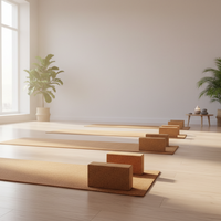 A minimalist yoga studio with several tan mats and matching wooden blocks arranged on a light wood floor, with potted plants near tall windows.
