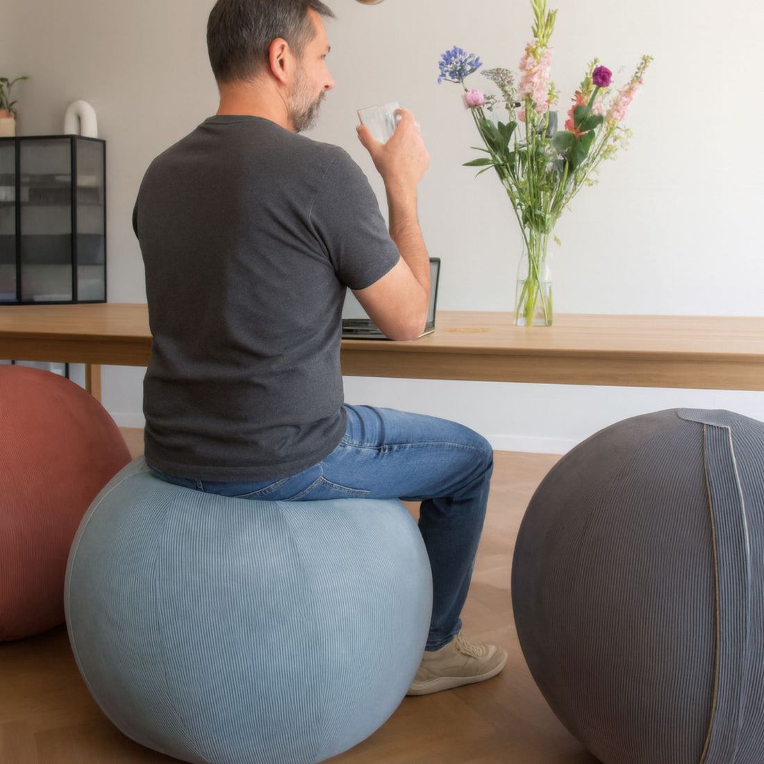 Man sitting on a balance ball in a home office setting with a desk and flowers.