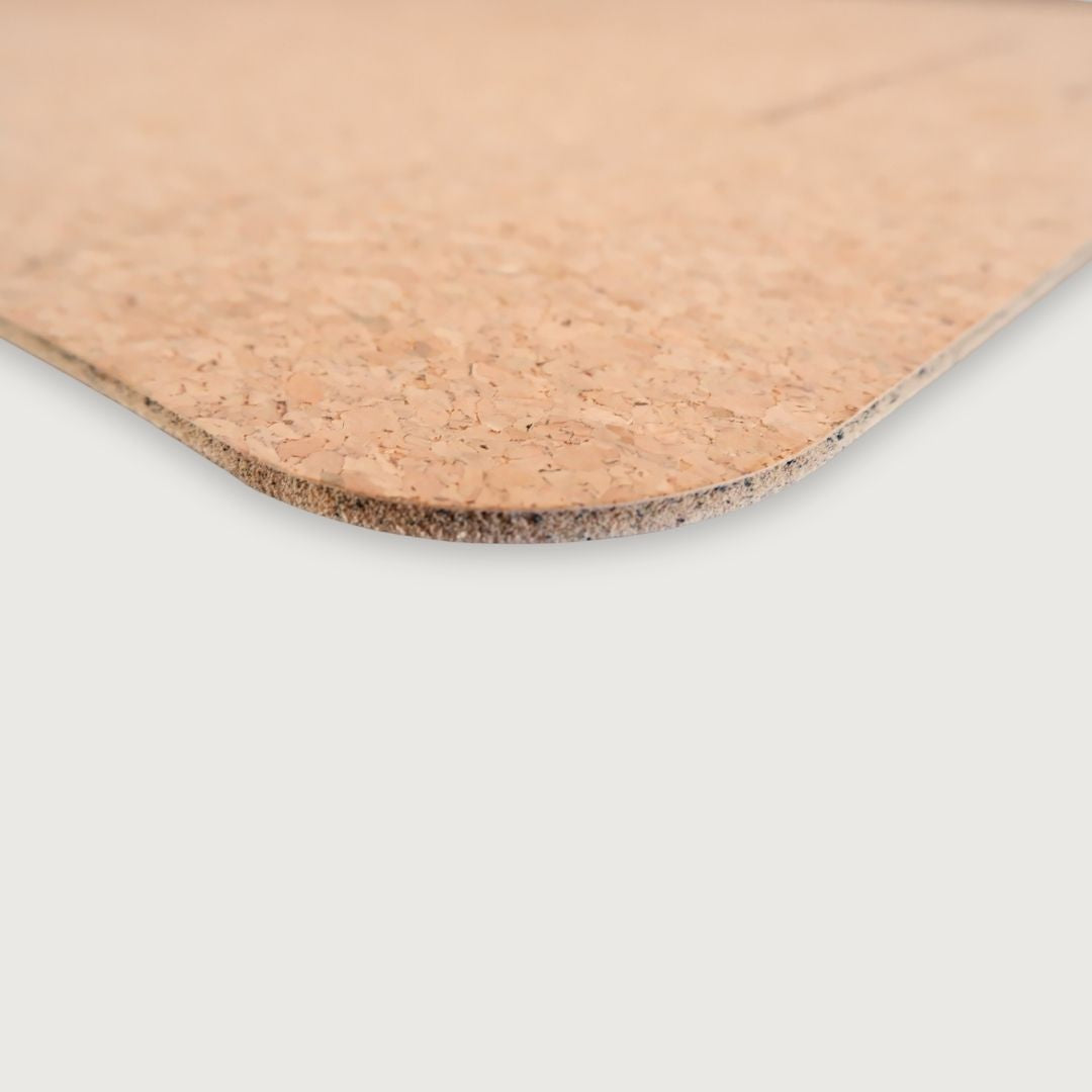 A close-up of a cork mat showing its natural tan cork texture and rounded corner, set against a solid light gray background.