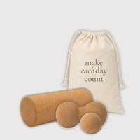 A cork massage set including a cylindrical cork roller, one round massage balls, a cork peanut roller and a natural canvas drawstring bag with the printed text 'make each day count', shown on a light gray background.