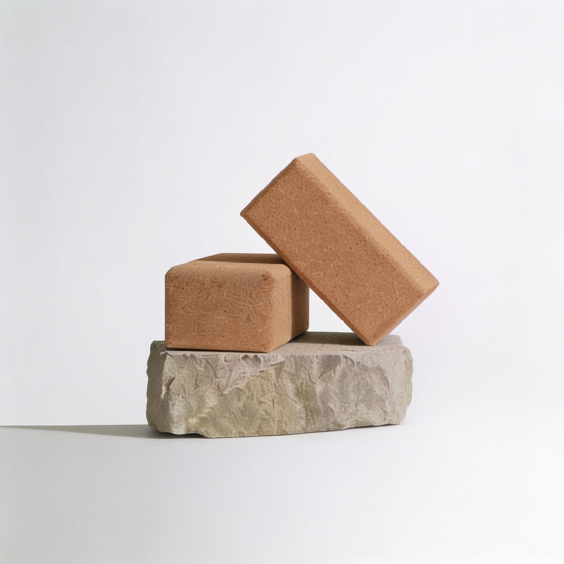 natural cork yoga blocks stacked and leaning on a textured stone base against a clean white background.